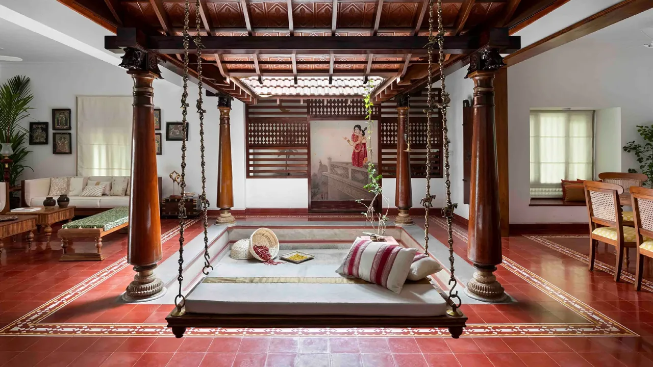 Traditional Kerala style farmhouse living room with carved teak wood furniture and a central courtyard view—heritage NRI home in Palakkad.